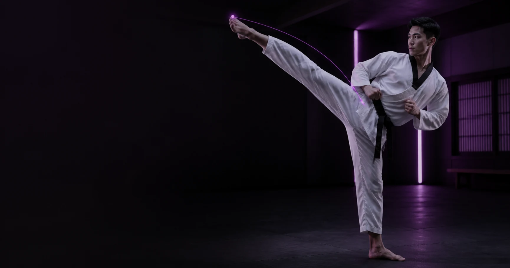 Taekwondo athlete extends a roundhouse kick under restrained magenta training light